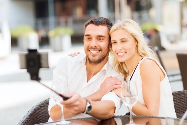 love, date, technology, people and relations concept - happy happy couple taking picture with smartphone on selfie stick at city street cafe or restaurant