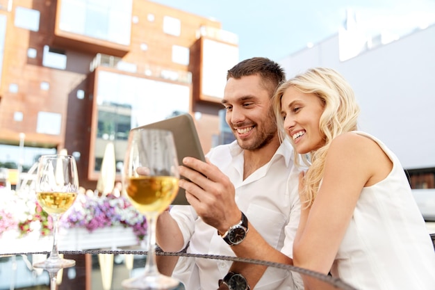 love, date, technology, people and relations concept - smiling happy couple with tablet pc computer at restaurant terrace