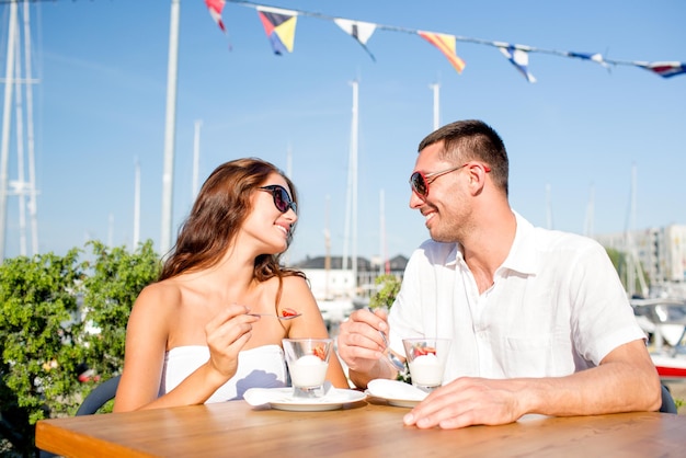 любовь, знакомства, люди и концепция еды - улыбающаяся пара в солнечных очках ест десерт и смотрит друг на друга в кафе