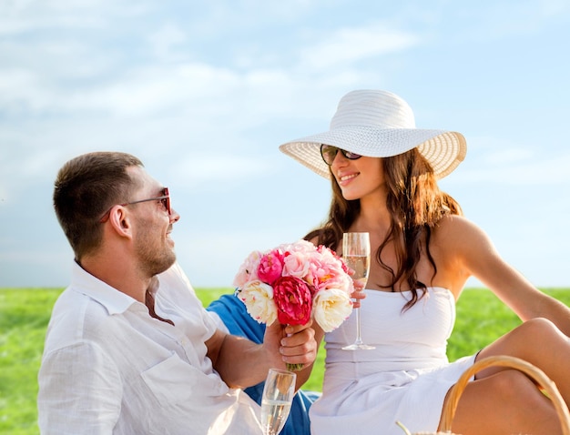 love, dating, people and holidays concept - smiling couple drinking champagne on picnic over blue sky and grass background