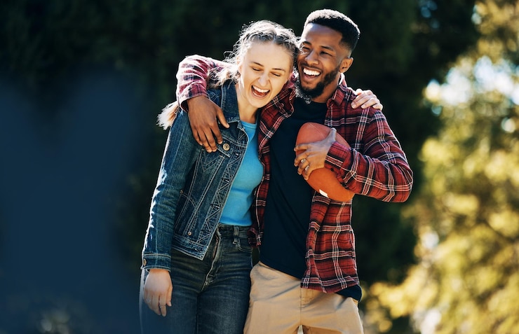 Photo love diversity couple and laughing in nature having fun and playing football outdoors comic interracial romance and happy black man and woman hug laugh at funny joke and enjoying time together