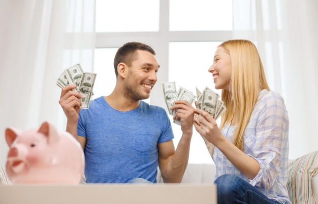 Foto concetto di amore, famiglia, finanza, denaro e felicità - coppia sorridente con denaro e salvadanaio a casa