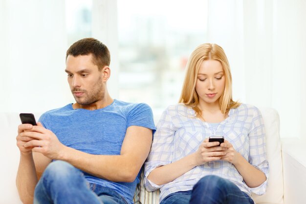 love, family, technology, internet and happiness concept - concentrated couple with smartphones at home