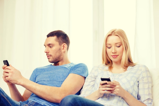 love, family, technology, internet and happiness concept - concentrated couple with smartphones at home