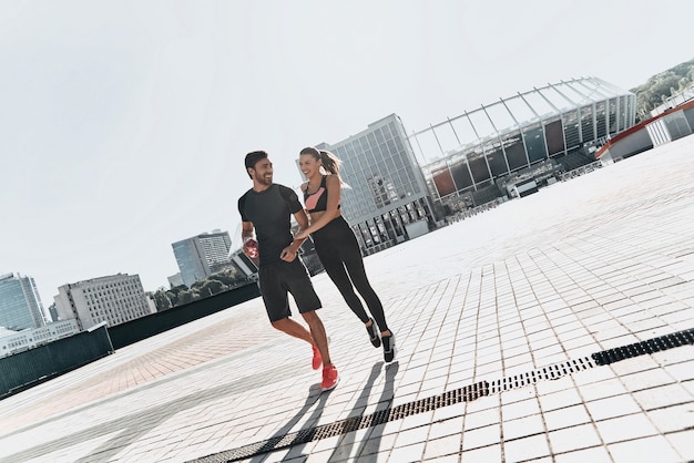 In love and full of energy. Full length of young couple in sport clothing bonding and smiling while walking outdoors