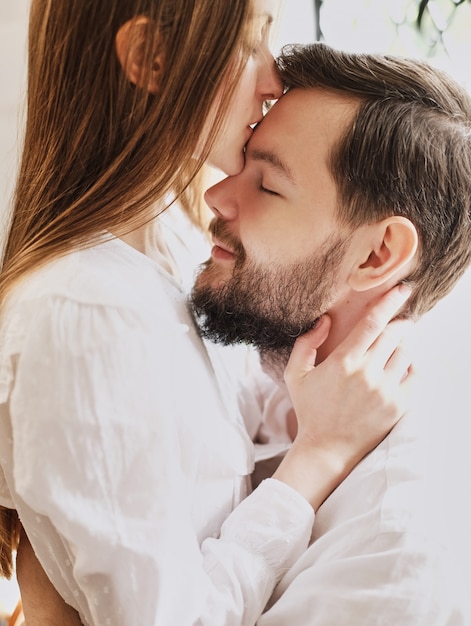 Foto la ragazza dell'amore bacia il suo ragazzo sulla fronte. abbracciare dolcemente il bacio. vestito in pigiama