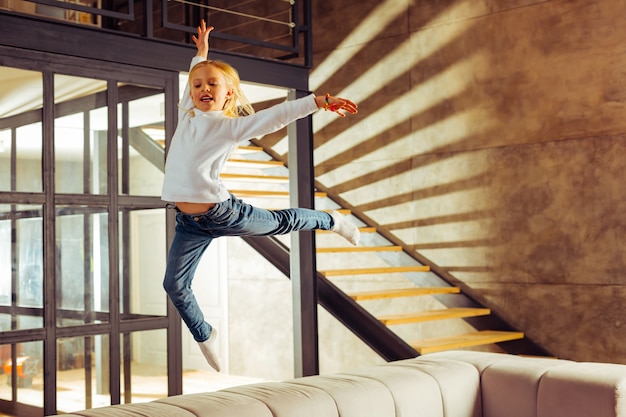 Love gymnastics. Cheerful kid keeping smile on her face while making effort in sport