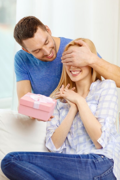 love, holiday, celebration and family concept - smiling man surprises his girlfriend with present at home