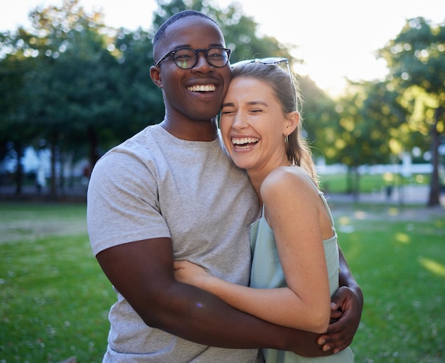 Love interracial or couple of friends hug in a park on a happy romantic date bonding in nature together Romance funny black man and woman laughing or enjoying quality time on a holiday vacation