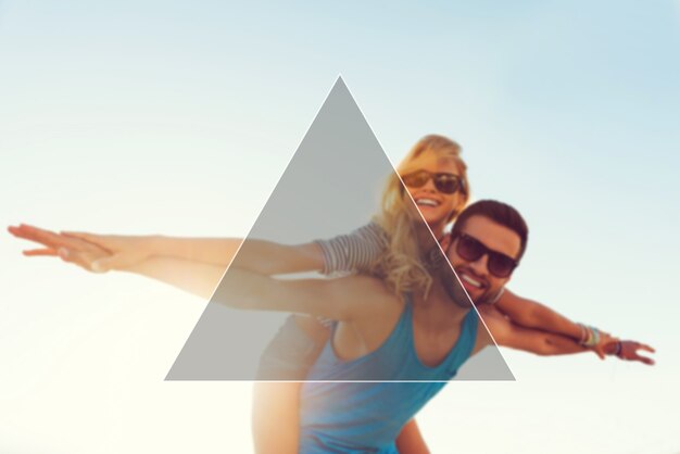 Love is in the air. Low angle view of smiling young man piggybacking his girlfriend while keeping arms outstretched