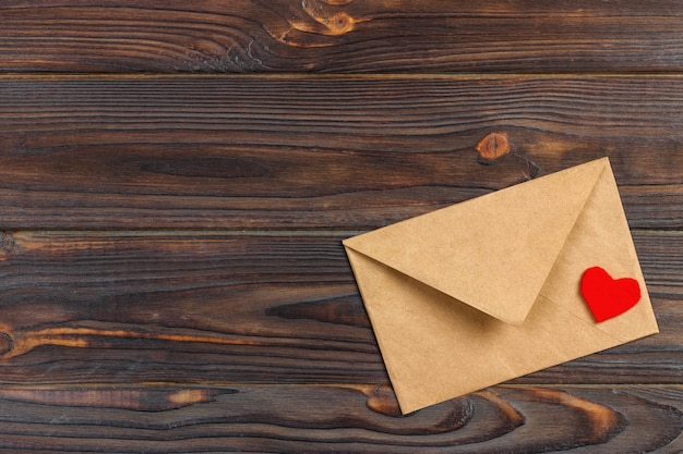 Love letter envelope with red heart on wooden background. 