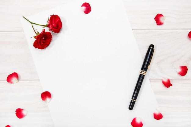 Love letter with red rose and petals on white wooden table