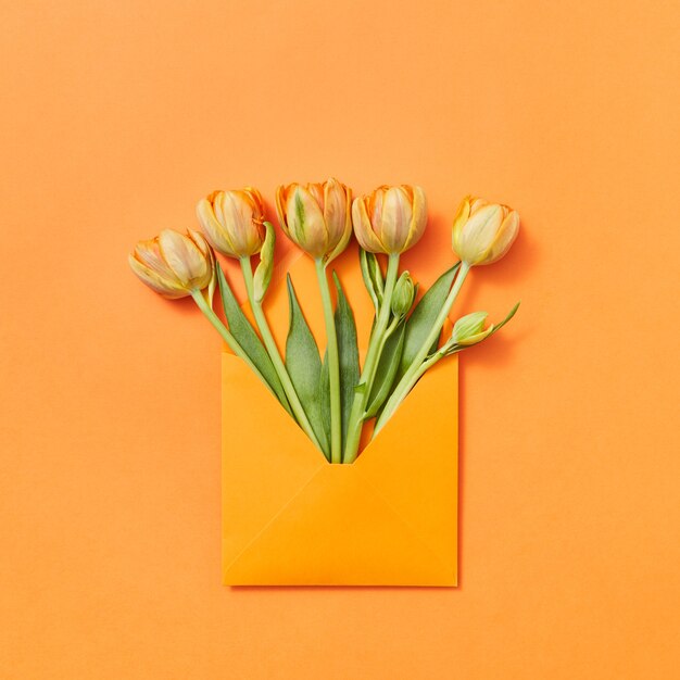 Love letter yellow freshly picked flowers in a handmade envelope on an orange background with lace for text. Flat lay.