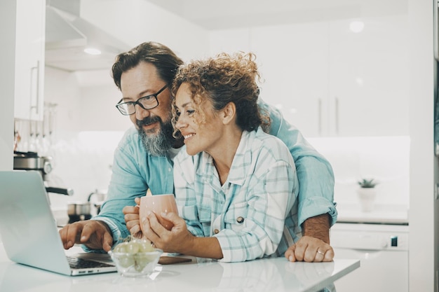 Love modern couple man and woman using together a laptop in the kitchen at home Online computer leisure activity people Happy family people enjoy time and surfing the web on computer Real life