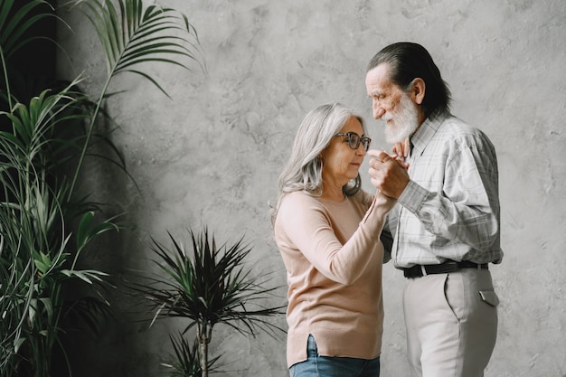 Love never grows old. Joyful active old retired romantic couple dancing in living room.