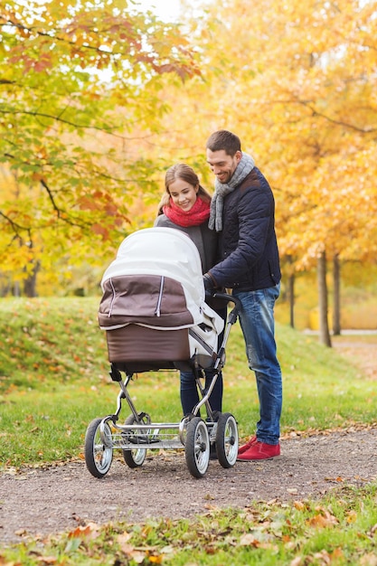 love, parenthood, family, season and people concept - smiling couple with baby pram in autumn park