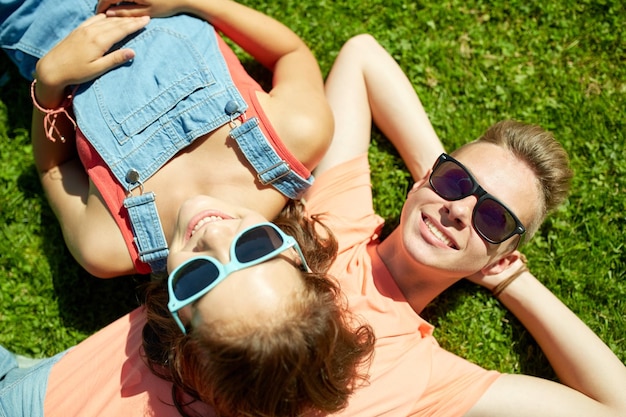 концепция любви и людей - счастливая пара подростков в солнечных очках, лежащих на траве летом