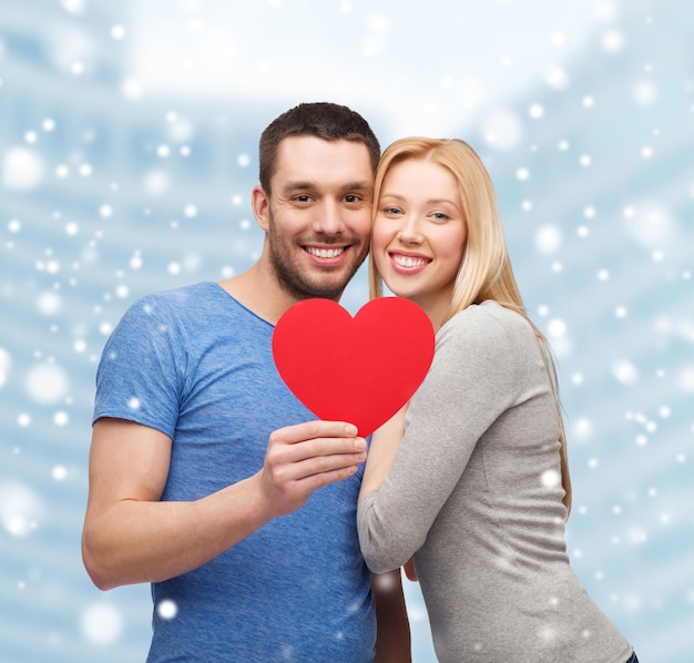 love, people and family concept - smiling couple with red paper heart shape hugging over snow and city buildings background