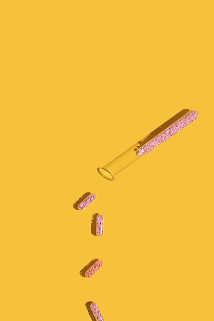 Love pills filled with pink heart shaped glitter falling out from a test tube on a yellow bright background with copy space. Valentine day minimal creative idea. Love breakup lab experiment concept.