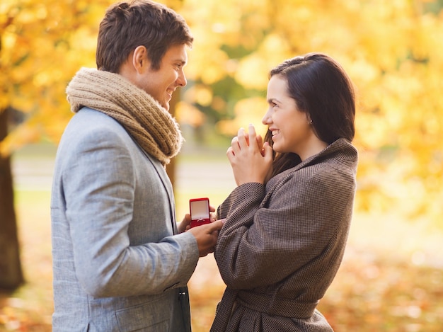 концепция любви, отношений, семьи и людей - улыбающаяся пара с красной подарочной коробкой в осеннем парке