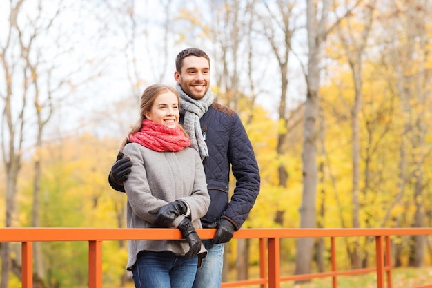 love, relationship, family, season and people concept - smiling couple hugging on bridge in autumn park