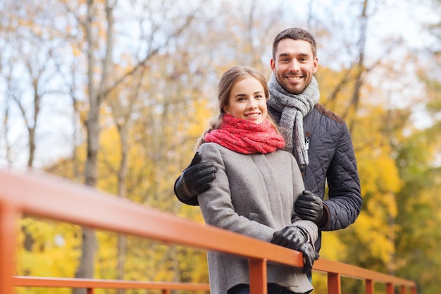 Concetto di amore, relazione, famiglia, stagione e persone - coppia sorridente che si abbraccia sul ponte nel parco autunnale