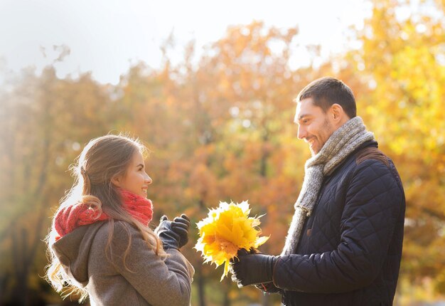 love, relationship, family, season and people concept - smiling couple with bunch of leaves in autumn park