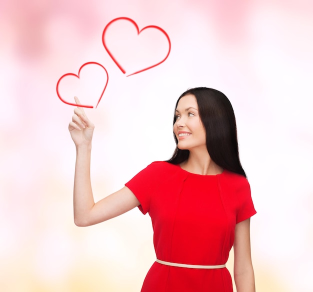 love, relationship and happiness concept - attractive young woman in red dress pointing her finger at hearts