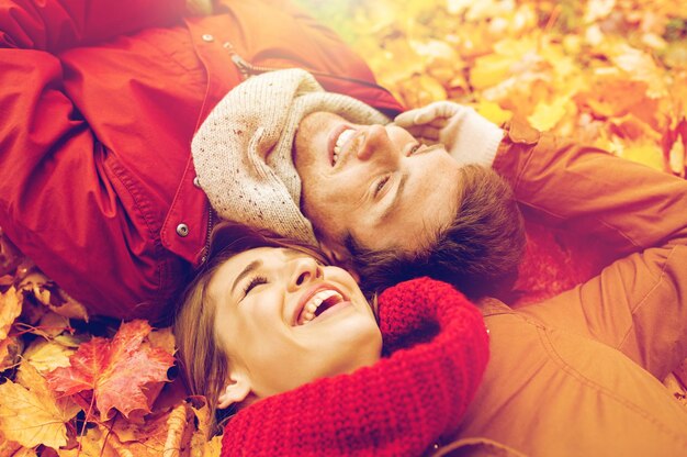 Фото Любовь, отношения, сезон, семья и люди концепция - крупный план улыбающейся пары, лежащей на осенних листьях