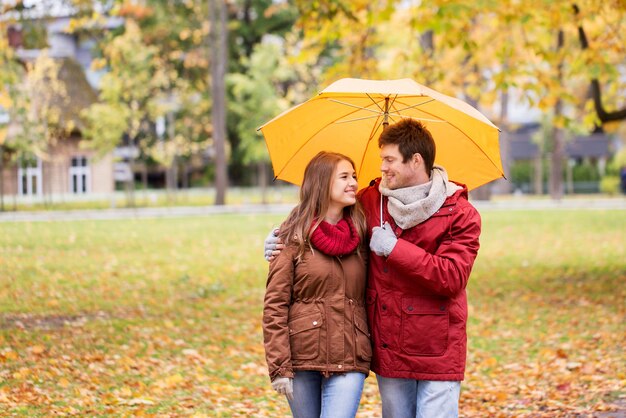 love, relationship, season, family and people concept - happy couple with umbrella walking in autumn park