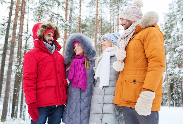 Concetto di amore, relazione, stagione, amicizia e persone - gruppo di uomini e donne sorridenti che parlano nella foresta invernale