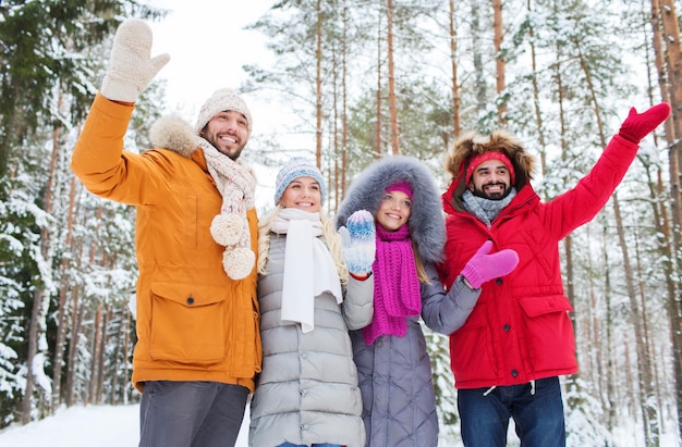 love, relationship, season, friendship and people concept - group of smiling men and women waving hands in winter forest