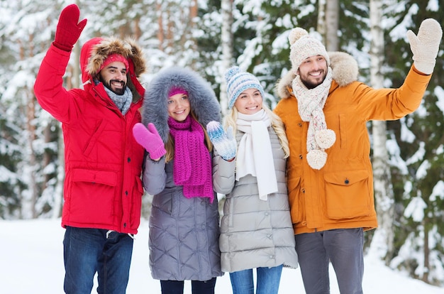 Concetto di amore, relazione, stagione, amicizia e persone - gruppo di uomini e donne sorridenti che agitano le mani nella foresta invernale