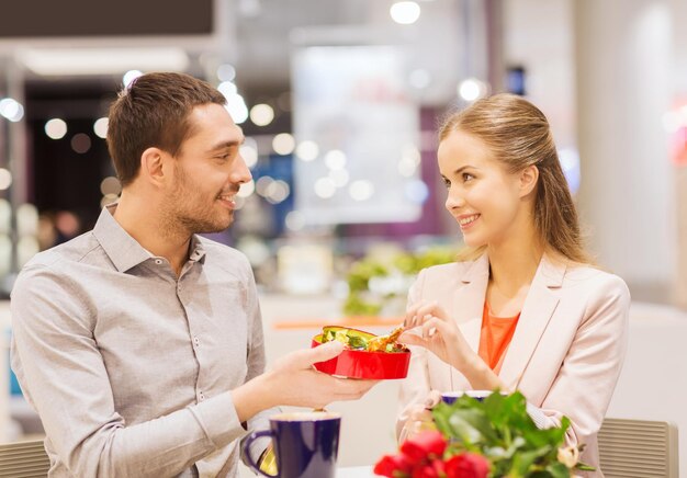 Concetto di amore, romanticismo, san valentino, coppia e persone - giovane coppia felice con fiori rossi e confezione regalo aperta al centro commerciale del caffè