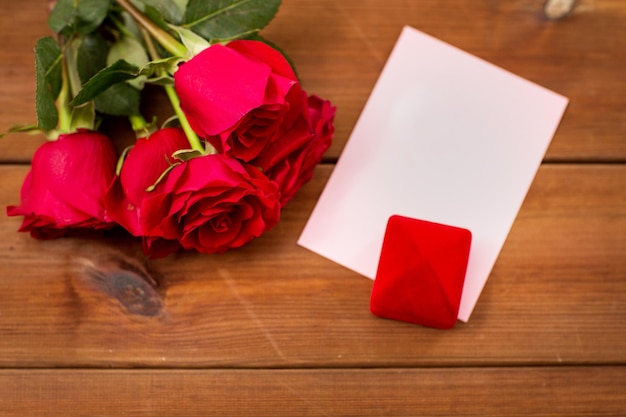 love, romance, valentines day and holidays concept - close up of gift box, red roses and greeting card on wood