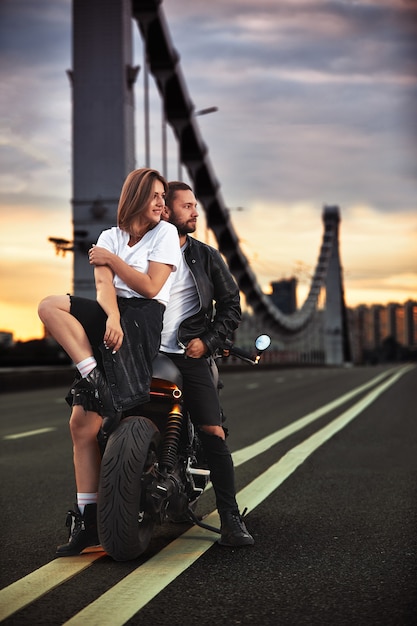 Photo love and romantic concept beautiful couple on motorcycle stands opposite each other in the middle of the road on the bridge, on double solid.