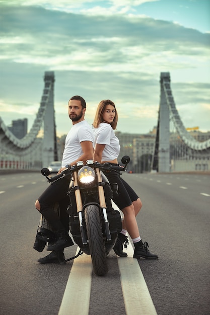 Photo love and romantic concept. beautiful couple on motorcycle stands opposite each other in the middle of the road on the bridge, on double solid.