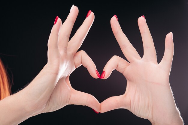 Photo love sign made by hands with red manicured nails on black