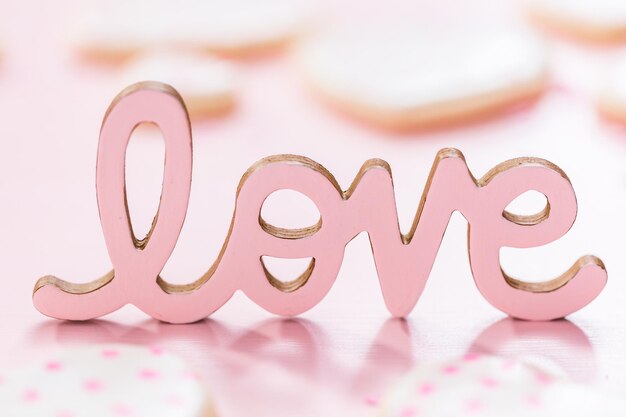 LOVE sign with heart shaped sugar cookies on a pink background.