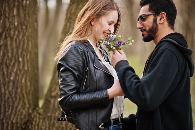 Love story of cool multiracial couple in spring forest Man gives flowers to his girlfriend