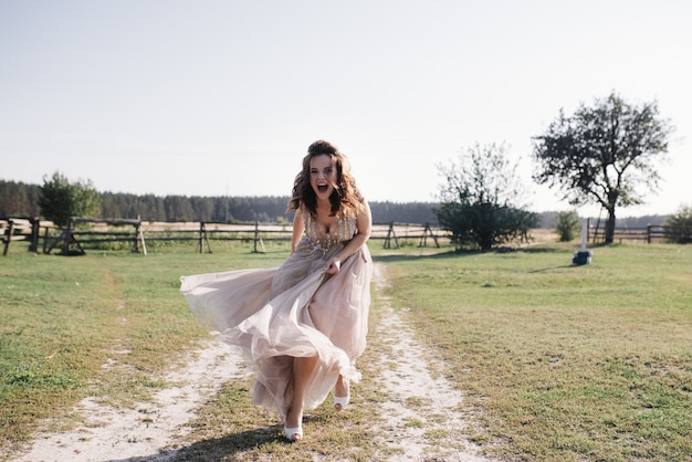 Love story and wedding near at sunset. The bride in a light airy dress is the color of a dusty rose. Beige dress with sparkles. The bride is running and smiling.