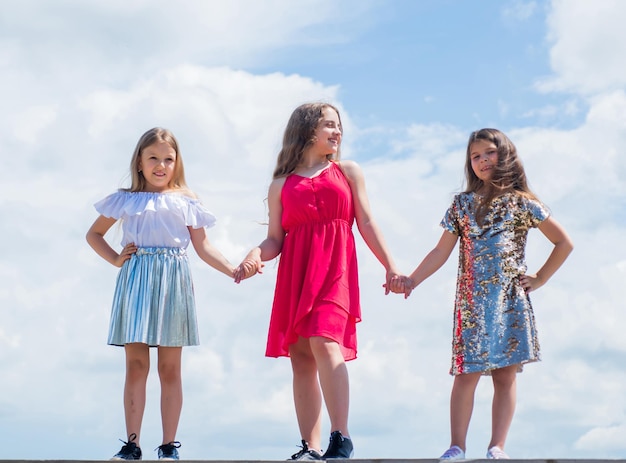 Love and support concept of sisterhood and friendship family bonding time best friends forever three sisters on sky background happy childhood concept summer vacation small girls hold hands