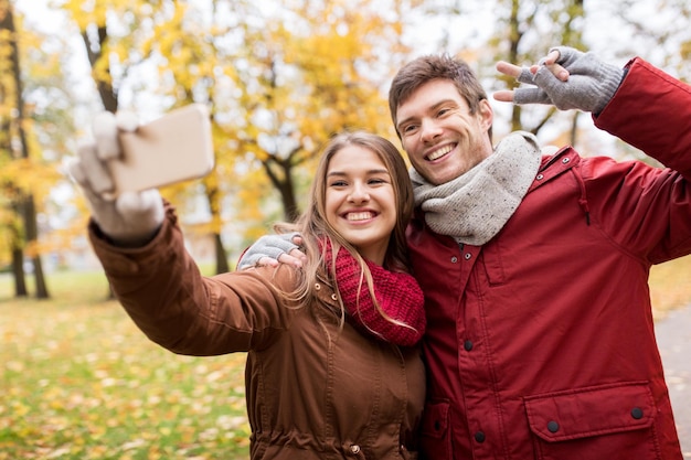 Photo love, technology, relationship, family and people concept - smiling couple taking selfie by smartphone in autumn park