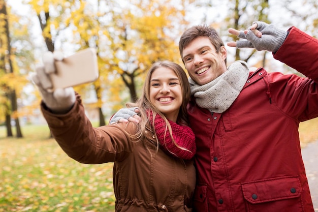 Love, technology, relationship, family and people concept - smiling couple taking selfie by smartphone in autumn park