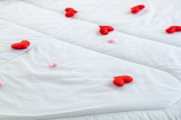 Love and Valentine Day Concept. Closeup of mini red and pink heart shape cloth pillow on white bed blanket.