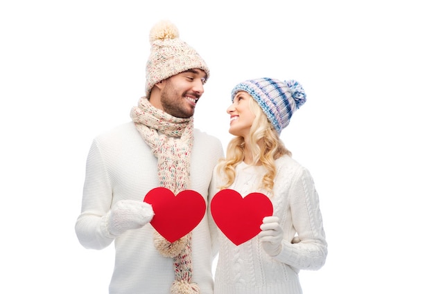 love, valentines day, couple, christmas and people concept - smiling man and woman in winter hats and scarf holding red paper heart shapes