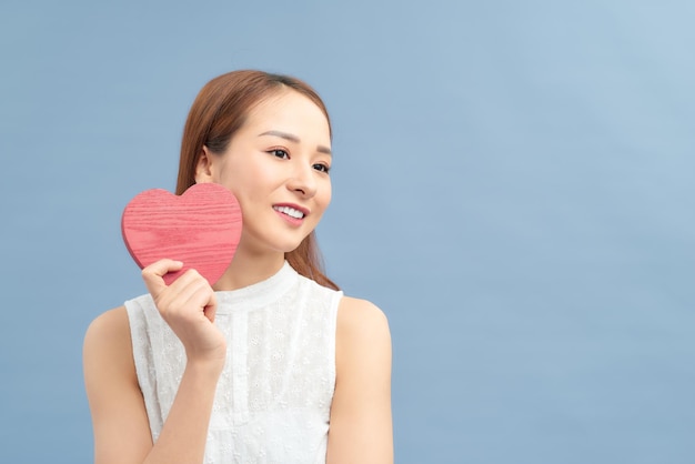 파란색 배경에 격리된 귀엽고 사랑스러운 미소를 짓고 있는 하트를 들고 있는 사랑과 발렌타인 데이 여성