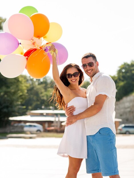 love, wedding, summer, dating and people concept - smiling couple wearing sunglasses with balloons hugging in park