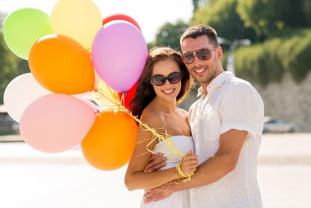 love, wedding, summer, dating and people concept - smiling couple wearing sunglasses with balloons hugging in park