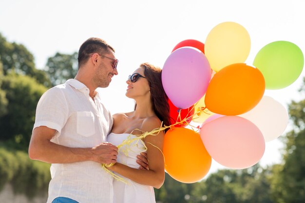 любовь, свадьба, лето, знакомства и концепция людей - улыбающаяся пара в солнечных очках с воздушными шарами, обнимающимися в парке